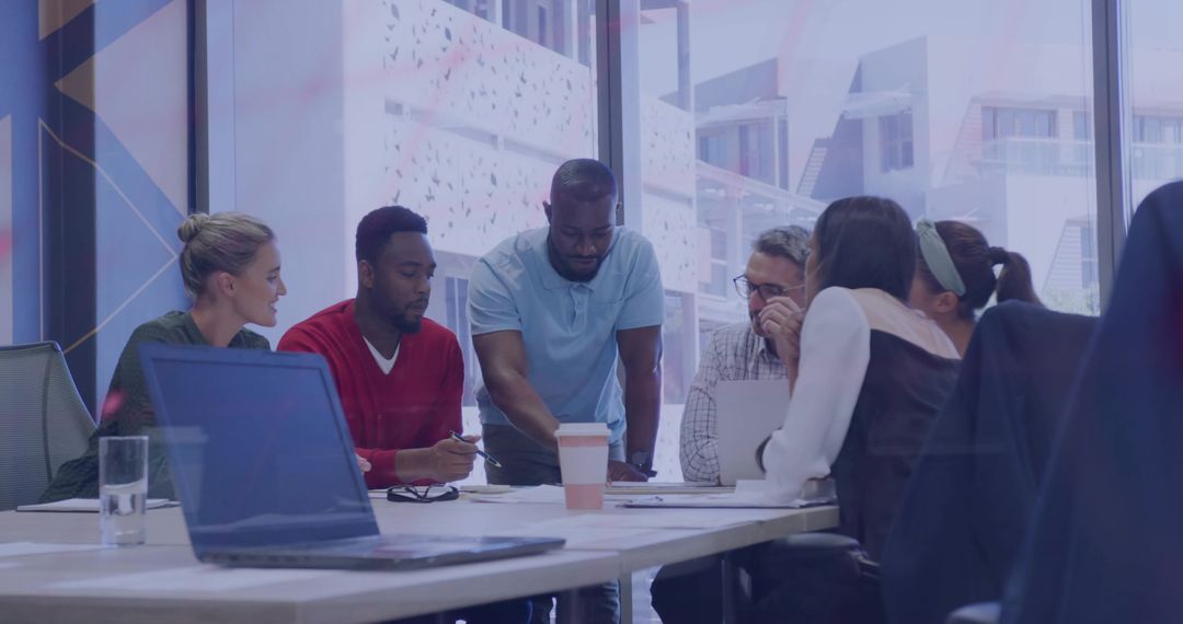 Diverse team collaborating around table reviewing laptop and documents in bright office