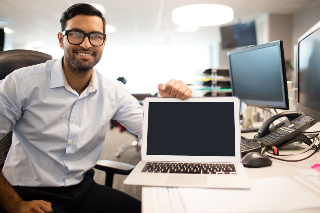 Smiling Businessman Showing Laptop at Office Desk - Free Images, Stock Photos and Pictures on Pikwizard.com