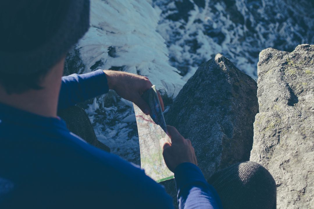 Hiker consulting topographic map on icy rocky summit planning mountain route navigation