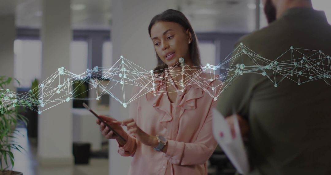 Woman presenting tablet with network overlay, collaborating with colleague in office