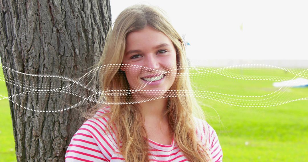 Smiling young woman leaning against tree with dotted wave overlay on sunny park lawn