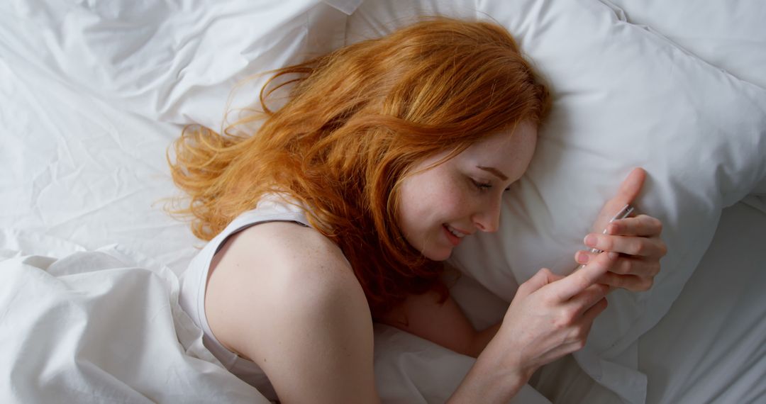 Redhead Woman Relaxing in Bed and Using Smartphone - Free Images, Stock Photos and Pictures on Pikwizard.com