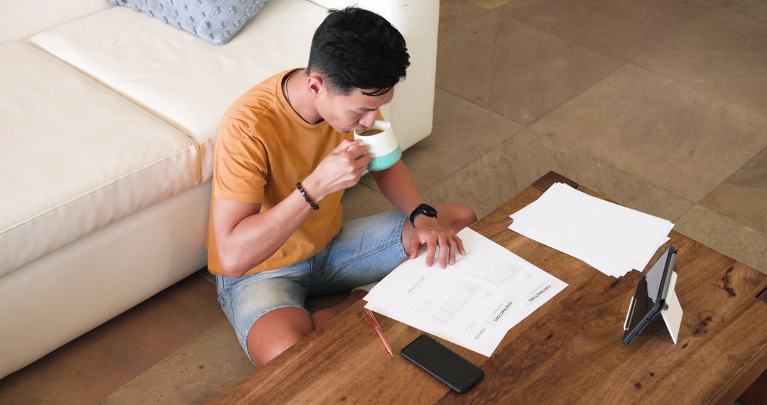 Young Man Reviewing Documents Beside Coffee Table at Home