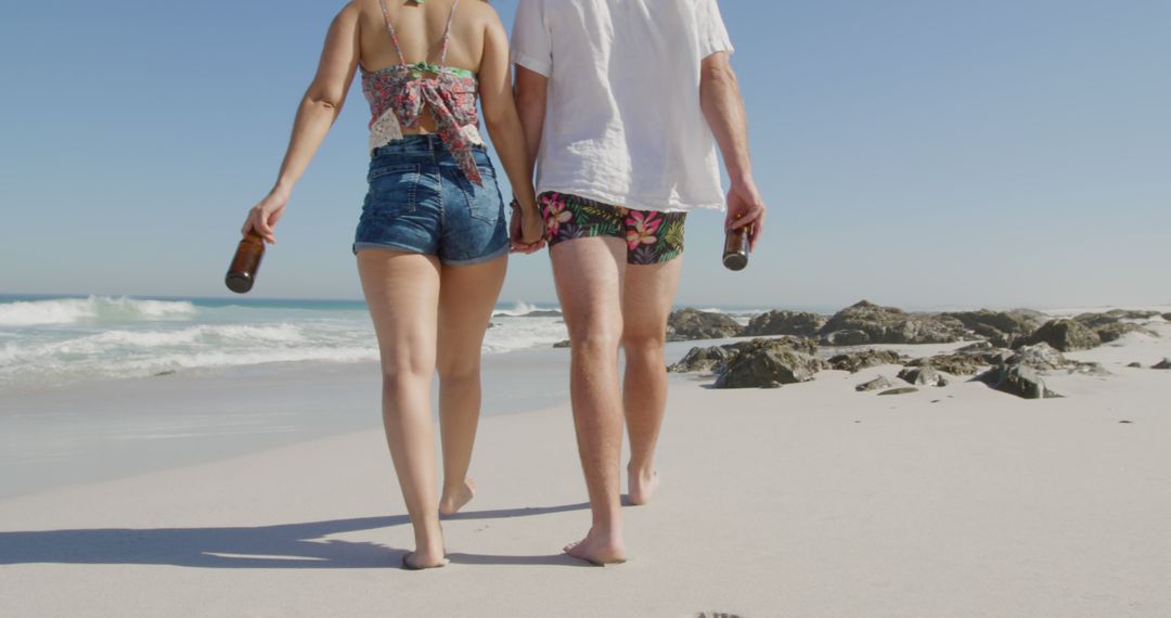 Couple Walking on Sunny Beach Holding Beer Bottles - Free Images, Stock Photos and Pictures on Pikwizard.com