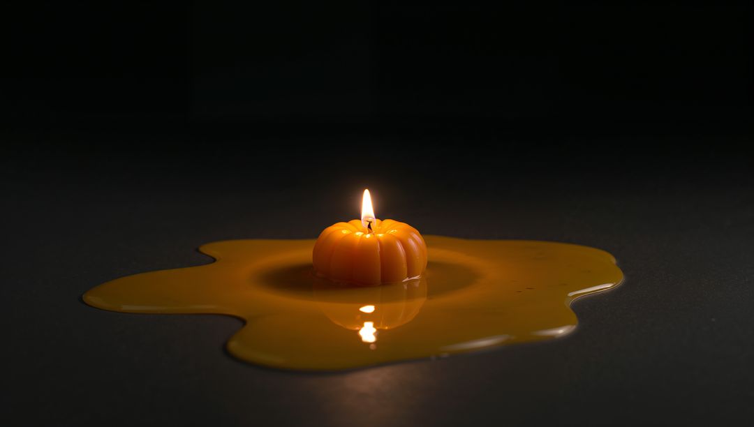 Pumpkin Candle Melting with Warm Reflections on Dark Surface