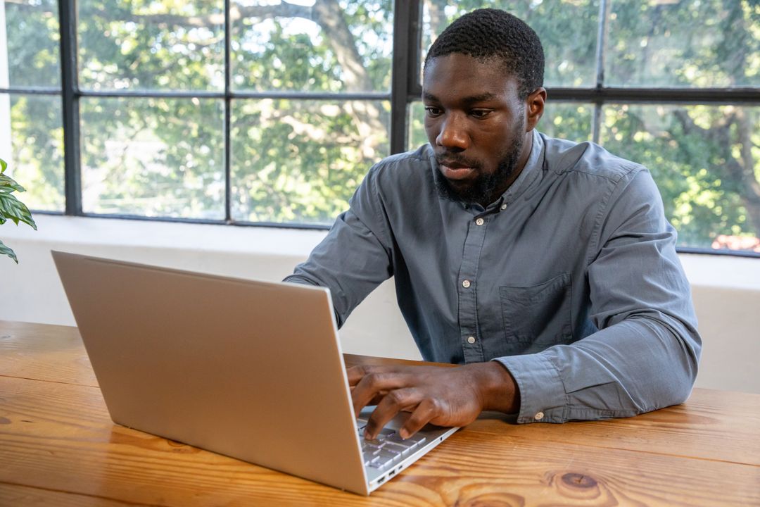 Focused Man Typing on Laptop in Bright Home Workspace