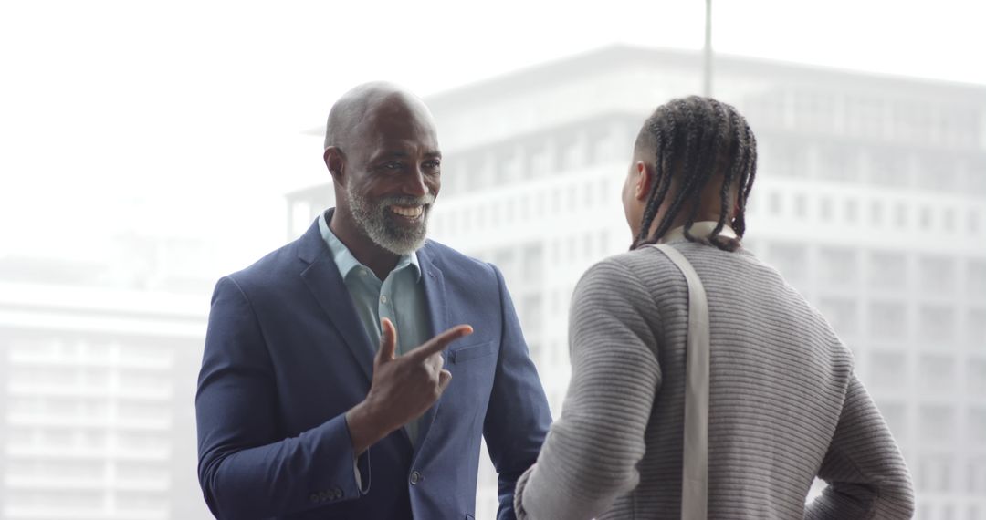 African American Mentor Pointing and Smiling with Young Colleague by Office Window