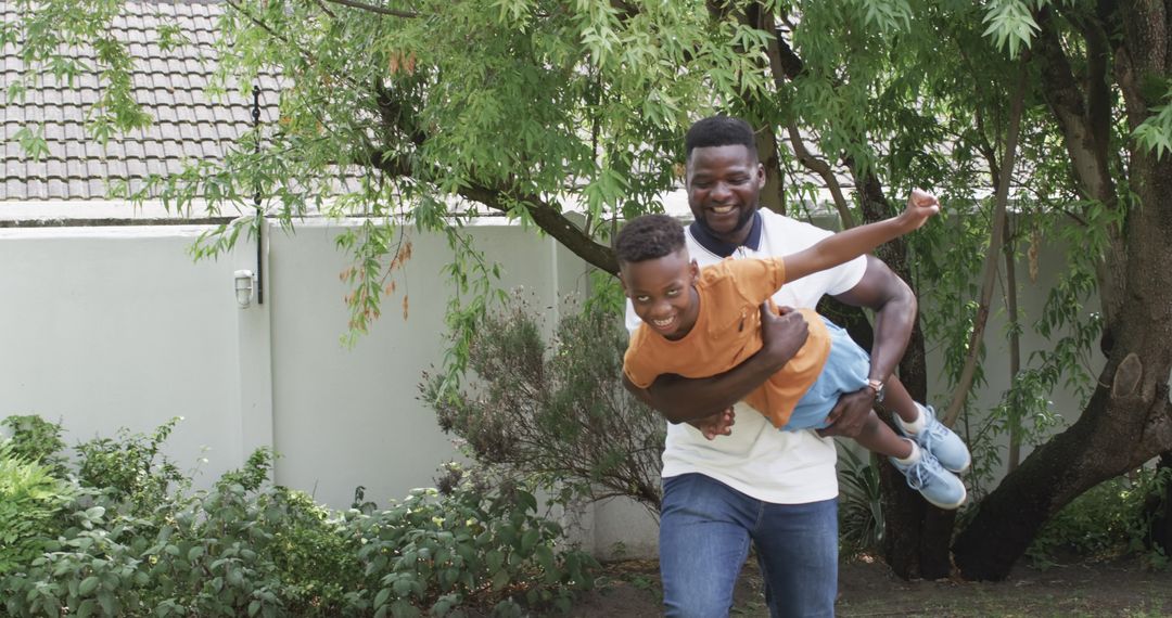 Father Giving Son Joyful Piggyback Ride in Green Backyard