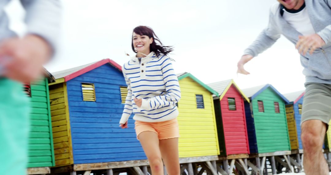 Group of Friends Running and Smiling Near Colorful Beach Huts - Free Images, Stock Photos and Pictures on Pikwizard.com