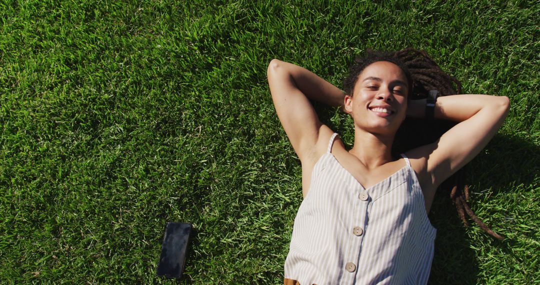 Happy woman with dreadlocks relaxing on grass in summer sun - Free Images, Stock Photos and Pictures on Pikwizard.com