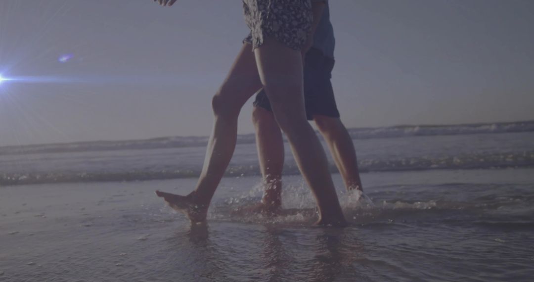 Couple Walking on Beach at Sunset with Waves Splashing
