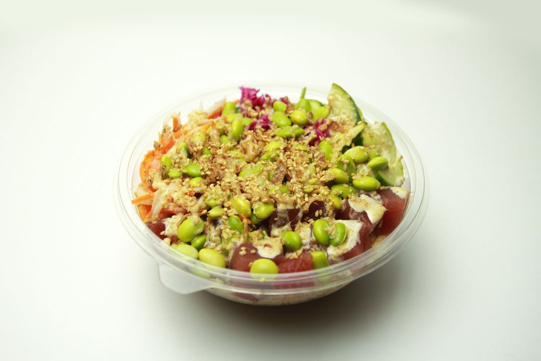 Fresh tuna poke bowl with edamame, sesame and mixed vegetables in clear takeout bowl