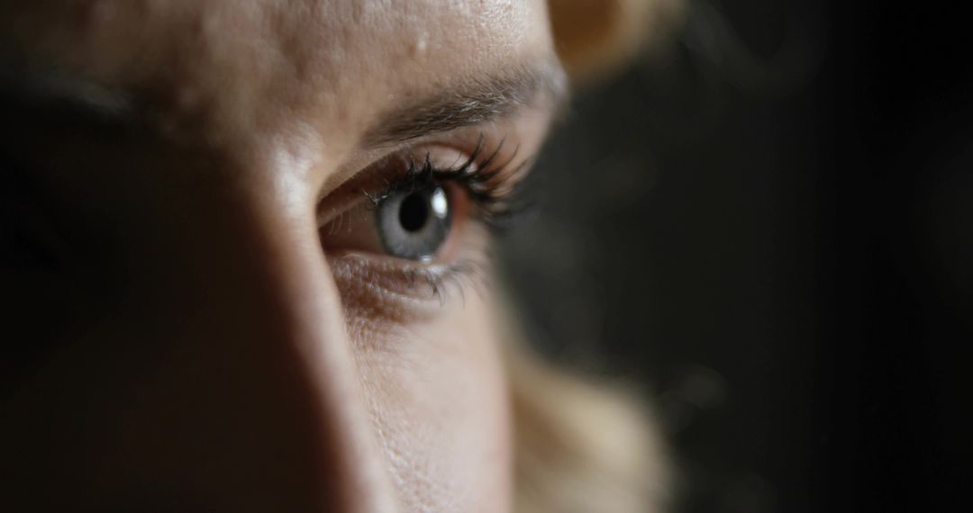 Gazing Close-Up of Female Eye Showing Iris, Eyelashes and Skin Texture in Soft Dim Light