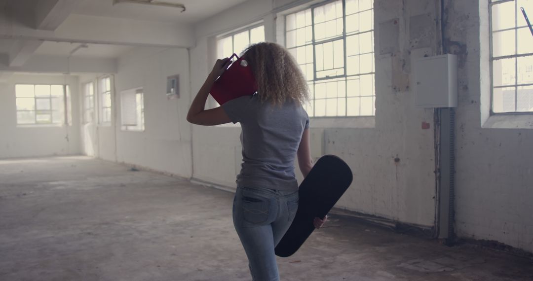 Woman with Afro Hair Carrying Skateboard in Industrial Warehouse - Free Images, Stock Photos and Pictures on Pikwizard.com