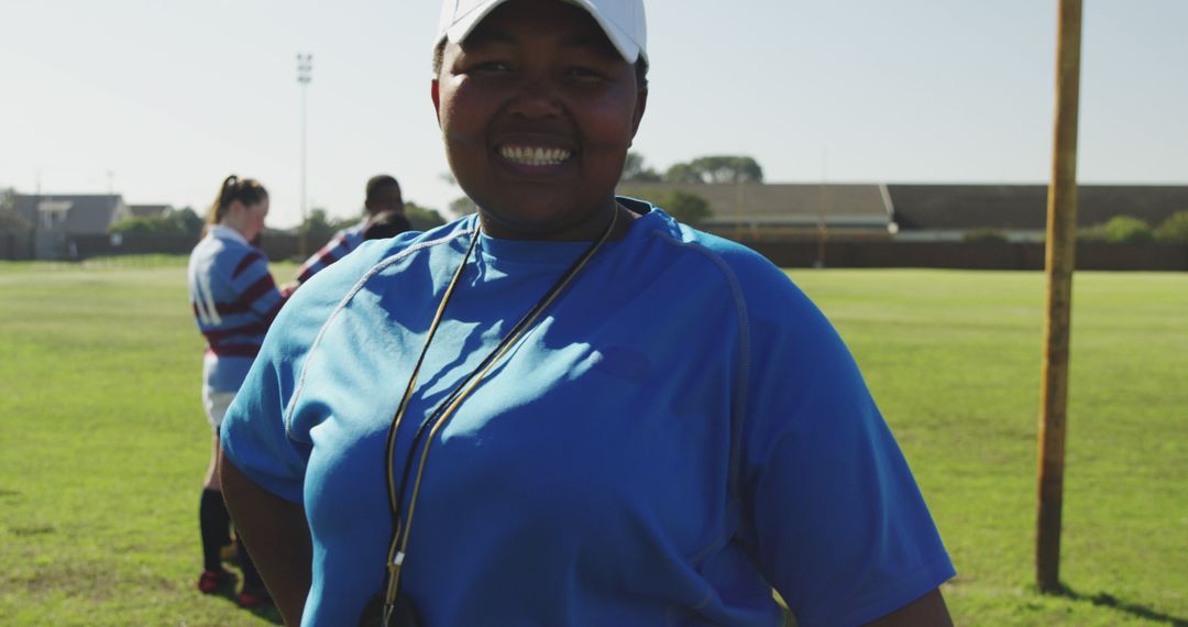 Portrait of happy african american female rugby trainer wearing cap with arms crossed on field - Free Images, Stock Photos and Pictures on Pikwizard.com