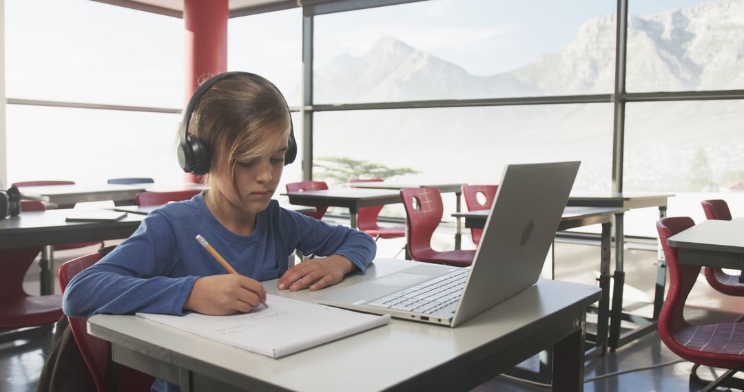 Focused Young Boy with Headphones Studying in Classroom with Laptop