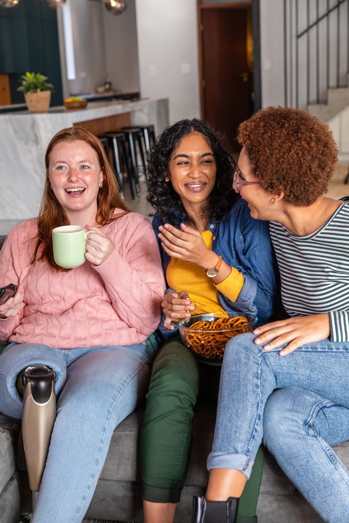 Diverse Female Friends Laughing and Relaxing on Sofa at Home