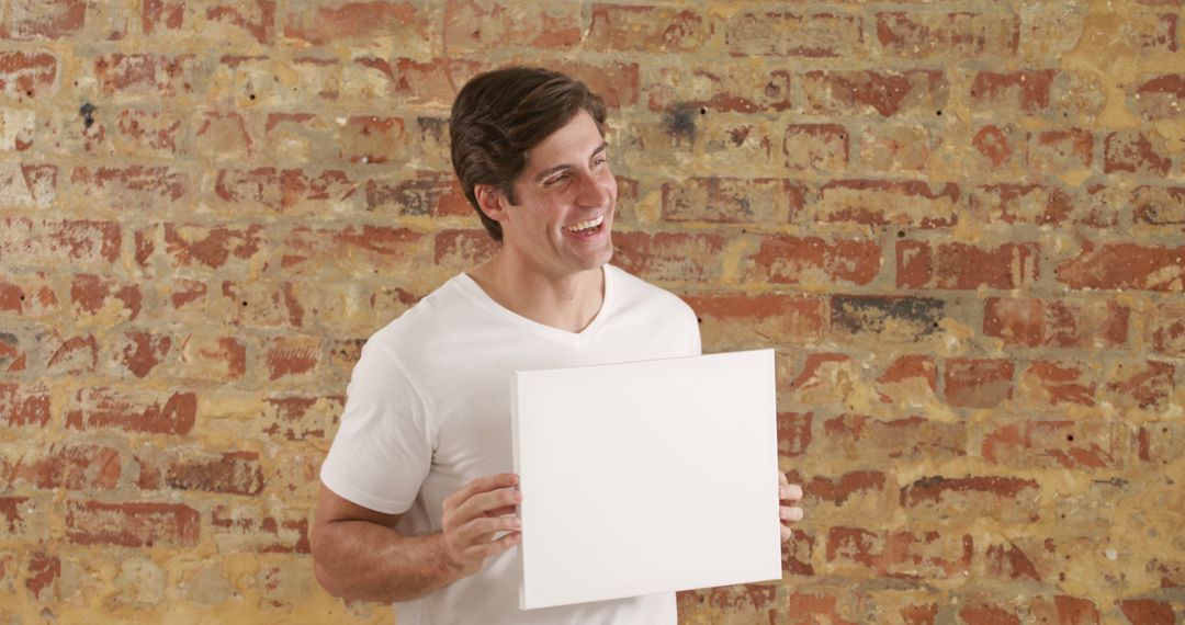 Smiling Man Holding Blank Cardboard in Front of Brick Wall - Free Images, Stock Photos and Pictures on Pikwizard.com