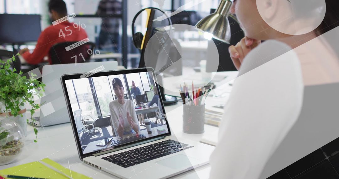 Watching remote team meeting on laptop with HUD analytics overlays in modern open office