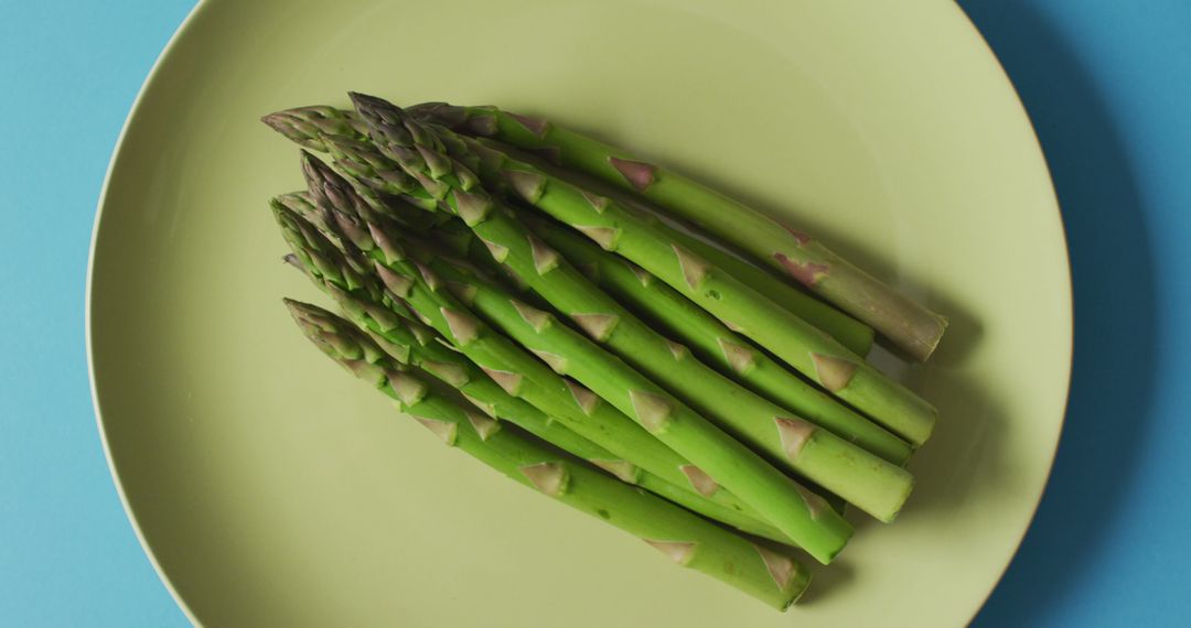 Image of fresh asparagus on green plate over blue background - Free Images, Stock Photos and Pictures on Pikwizard.com