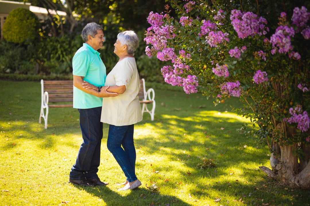 Biracial senior couple gazes lovingly by park flowers, side view - Free Images, Stock Photos and Pictures on Pikwizard.com