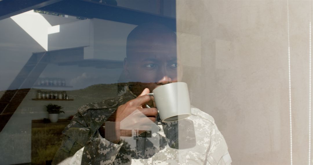 Soldier in Uniform Looking Through Window While Holding Coffee Mug