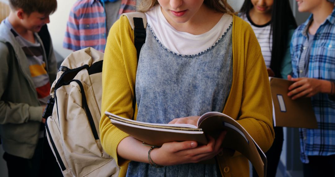 Teen Student Reading Book While Standing with Friends in Background - Free Images, Stock Photos and Pictures on Pikwizard.com