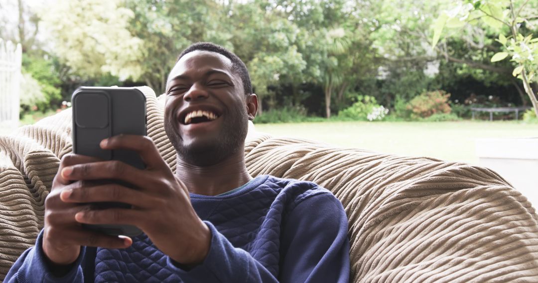 Joyful Young Man Laughing While Using Smartphone Outdoors