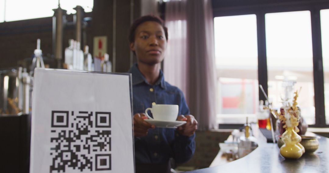 Barista holding cup presenting coffee while standing by QR code sign in coffee shop - Free Images, Stock Photos and Pictures on Pikwizard.com