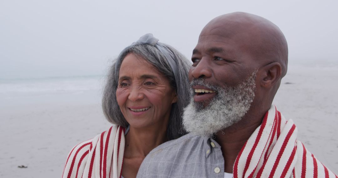 Smiling Senior Couple Wrapped in Blanket Enjoying Beach Serenity - Free Images, Stock Photos and Pictures on Pikwizard.com