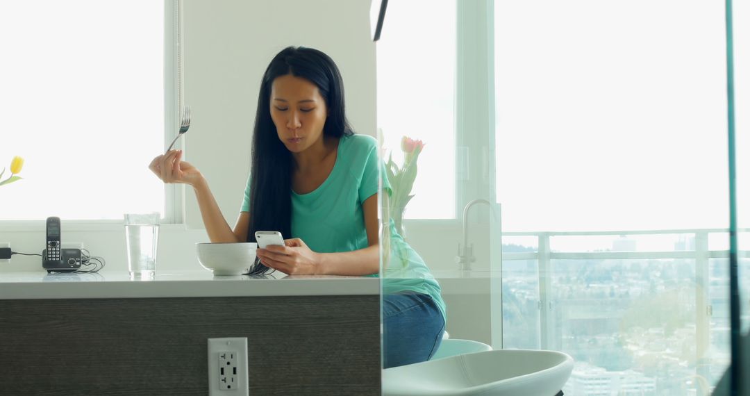 Woman Eating Breakfast While Browsing Smartphone in Modern Kitchen - Free Images, Stock Photos and Pictures on Pikwizard.com