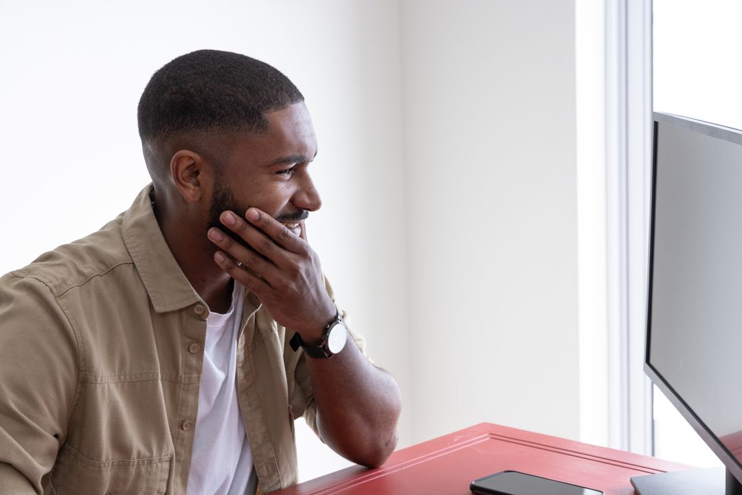 Man Focusing on Computer Work at Red Desk in Minimalist Home Office