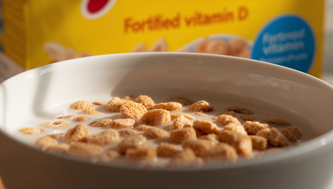 Crunchy toasted cereal floating in milk in white bowl with blurred fortified vitamin D box