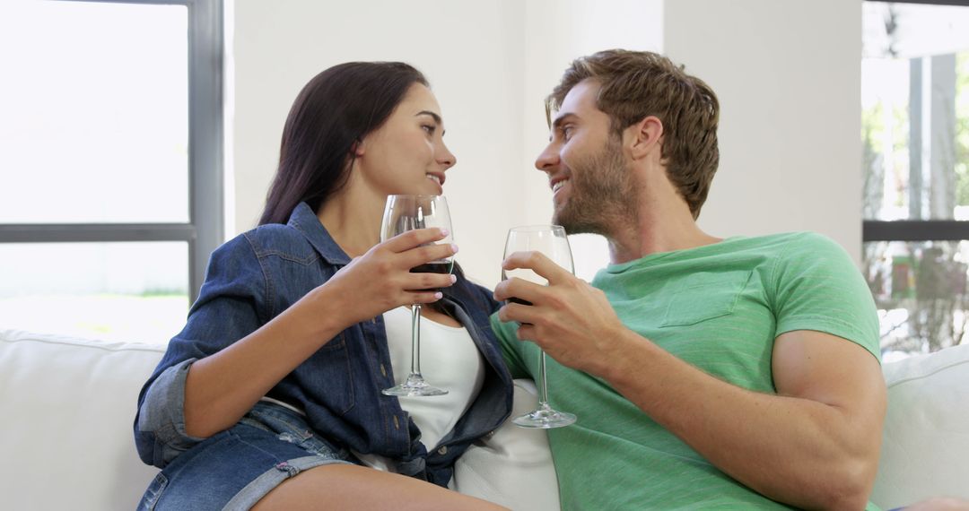 Couple Sitting on Couch Smiling at Each Other While Drinking Wine - Free Images, Stock Photos and Pictures on Pikwizard.com