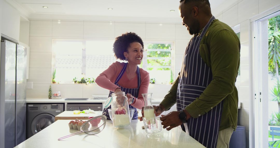 Couple baking together in bright modern kitchen pouring milk and measuring flour at island