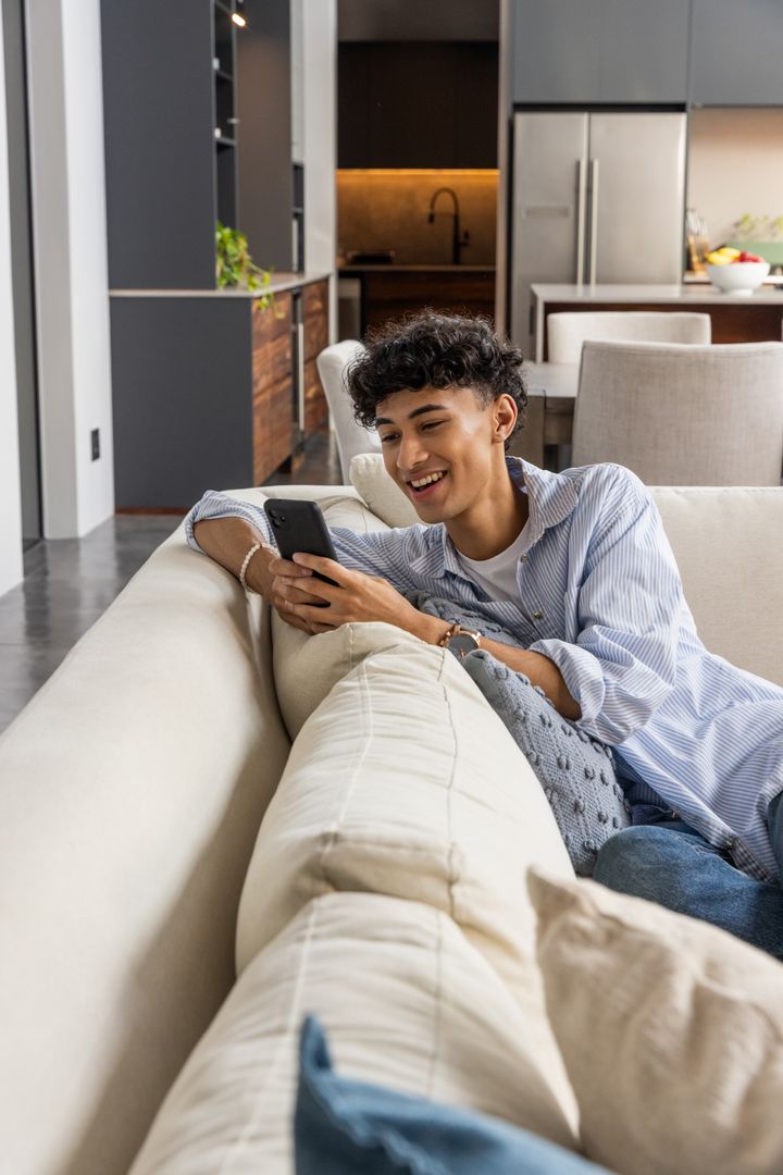 Relaxed Man Enjoying Smartphone on Modern Sofa in Minimalistic Home