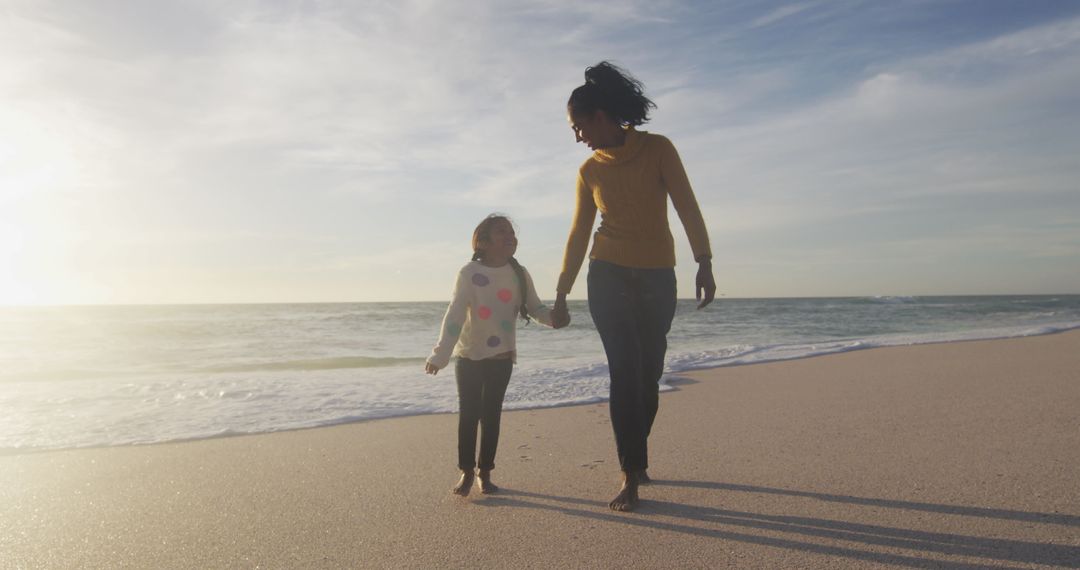 Mother and Daughter Walking on Sandy Beach at Sunset