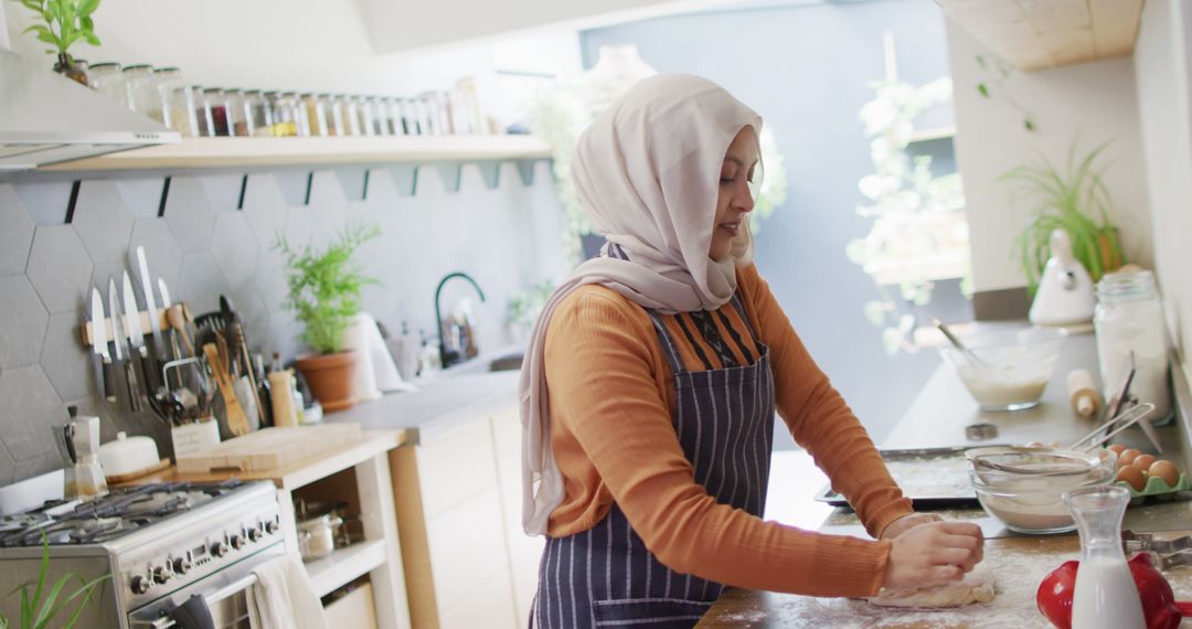 Image of happy biracial woman in hijab baking in kitchen at home, kneading dough - Free Images, Stock Photos and Pictures on Pikwizard.com