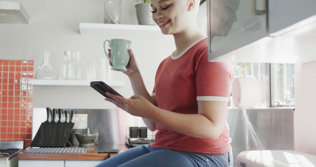 Smiling Young Woman Drinking Coffee and Using Smartphone in Modern Kitchen - Free Images, Stock Photos and Pictures on Pikwizard.com