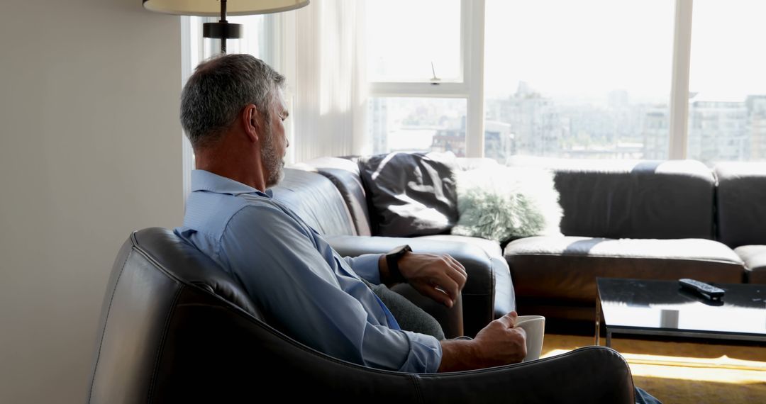 Man Relaxing on Couch Holding Coffee Mug in Modern Sunlit Living Room - Free Images, Stock Photos and Pictures on Pikwizard.com