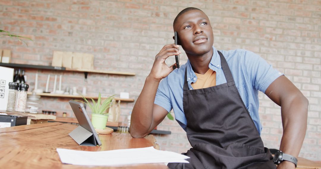 African American Man in Apron Smiling While Talking on Phone in Cafe - Free Images, Stock Photos and Pictures on Pikwizard.com