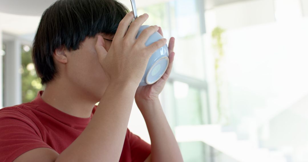 Asian Student Drinking from Cup in Relaxed Home Environment