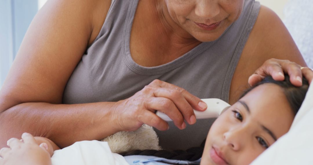 A mother uses an ear thermometer to check her daughter's temperature, showing care. - Free Images, Stock Photos and Pictures on Pikwizard.com