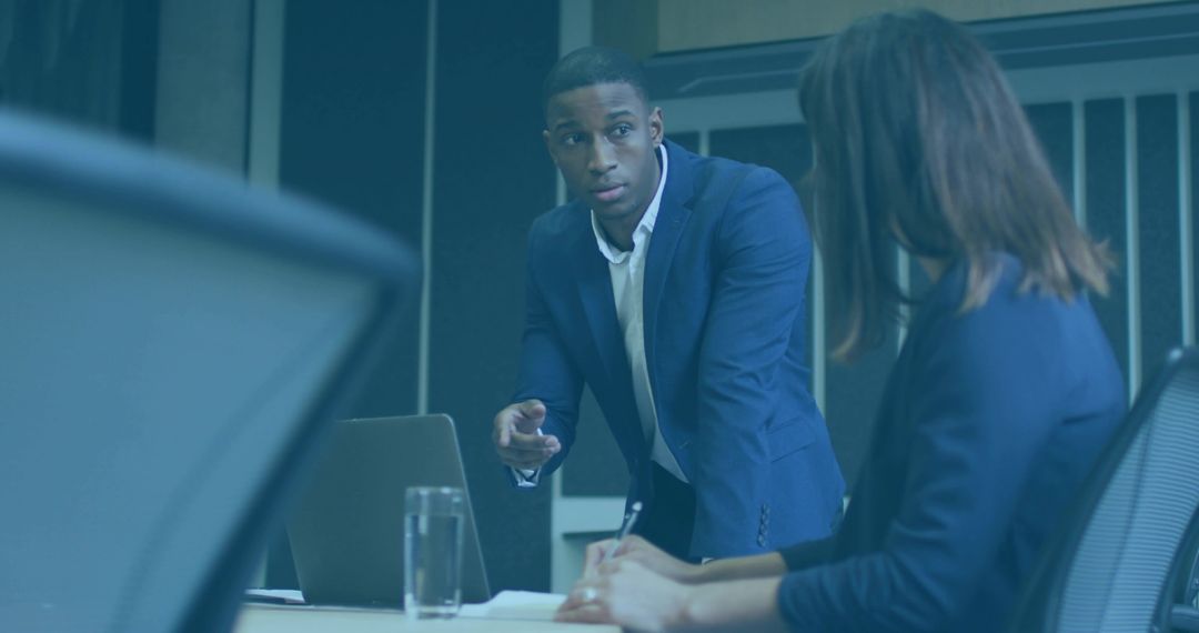 Executive Leading Discussion Leaning Over Conference Table Pointing While Colleague Taking Notes