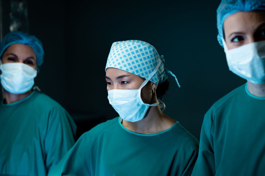 Three diverse female surgeons in face masks and caps during surgery in operating theatre - Free Images, Stock Photos and Pictures on Pikwizard.com
