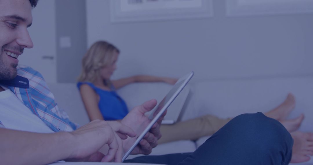 Young Couple Relaxing on Couch While Using Tablet and Laptop for Casual Home Browsing