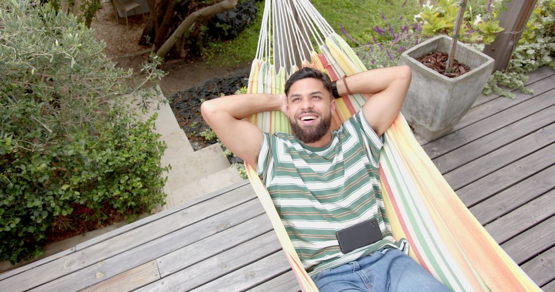 Young Man Relaxing in Hammock with Smartphone in Garden