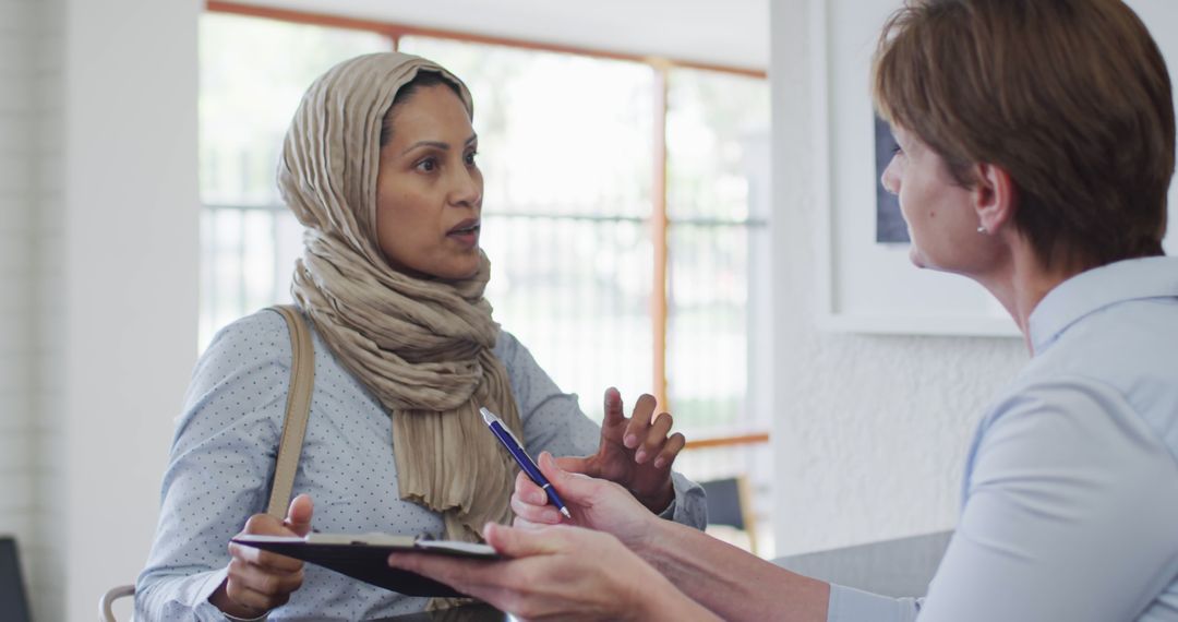 Hijab-Wearing Woman Discussing with Colleague in Office - Free Images, Stock Photos and Pictures on Pikwizard.com