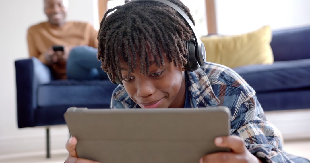 African-American Child Using Tablet with Headphones, Relaxing Home Environment - Free Images, Stock Photos and Pictures on Pikwizard.com