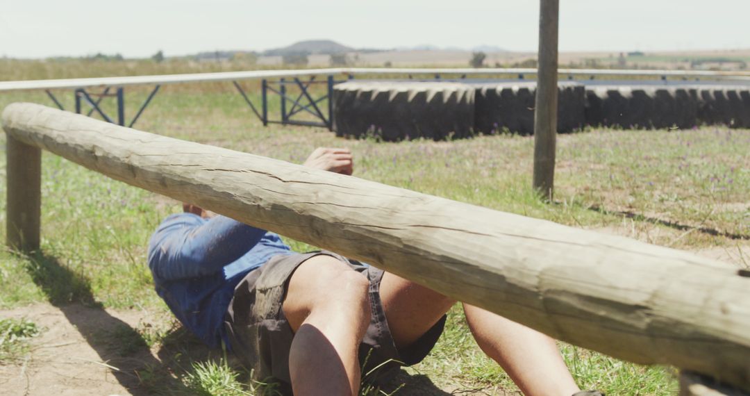 Man Crawling Under Wooden Obstacle on Outdoor Course